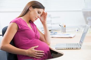 Pregnant lady sitting with a laptop looking stressed