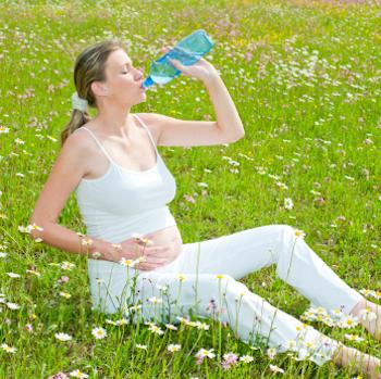 Pregnant lady drinking from a water bottle sitting in a field