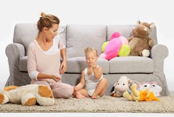 Mother and child playing together on a rug in front of a sofa and a pile of soft toys.