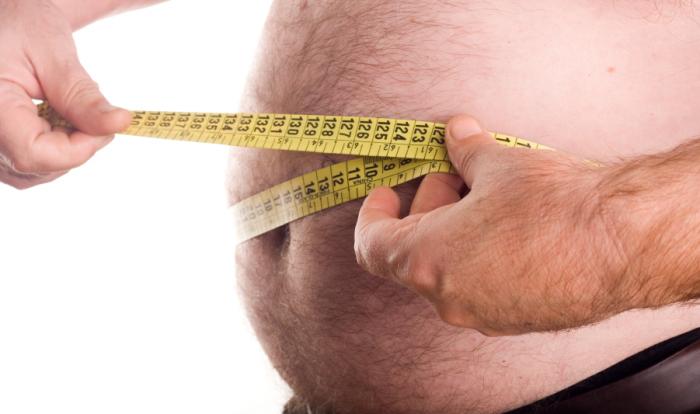 An overweight man measuring his waist